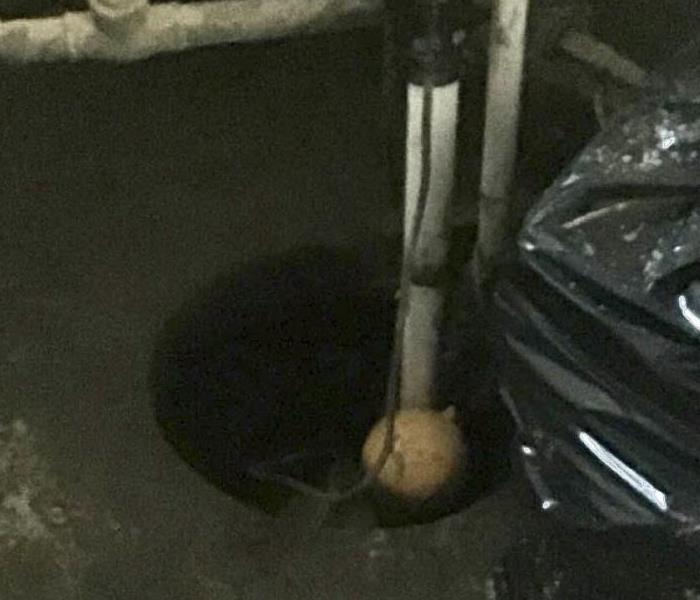 A photo showing heavy mud surrounding a sump pump in a basement