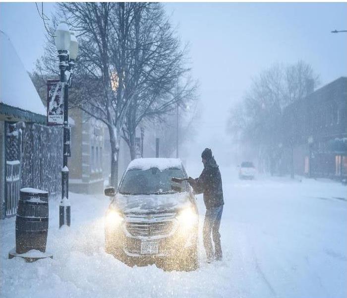 A man brushing snow from his car in a storm